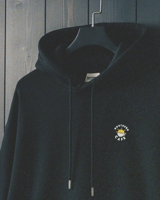 Black hoodie with a logo on a hanger against a wooden background