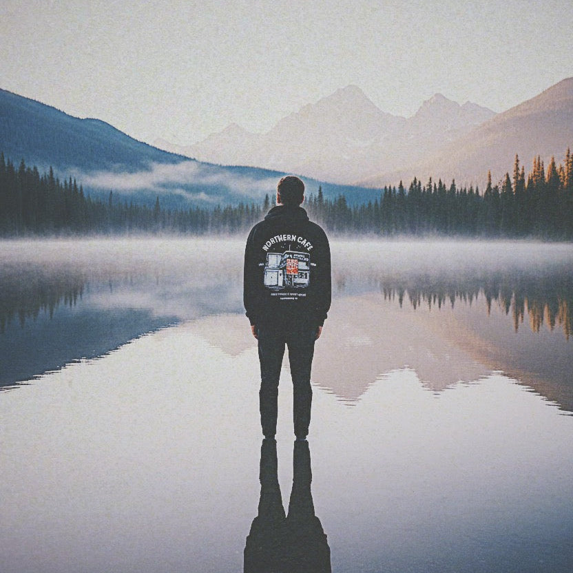 Person standing on a reflective lake with mountains in the background