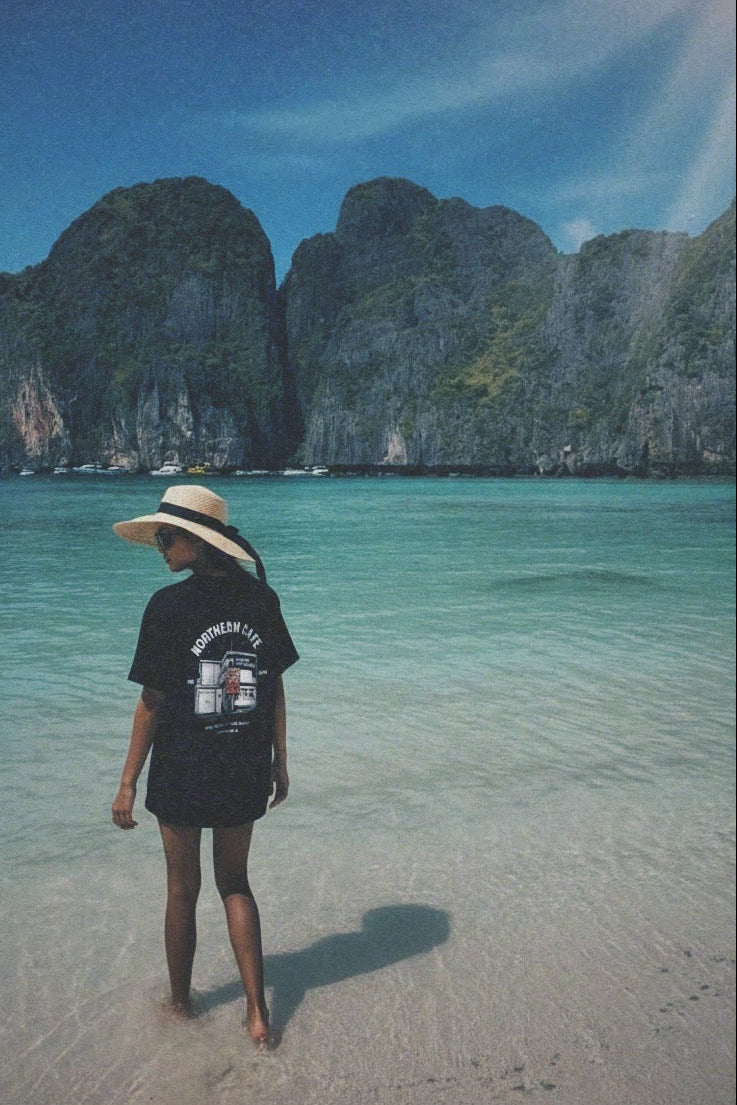 Person standing on a sandy beach with clear water and rocky cliffs in the background
