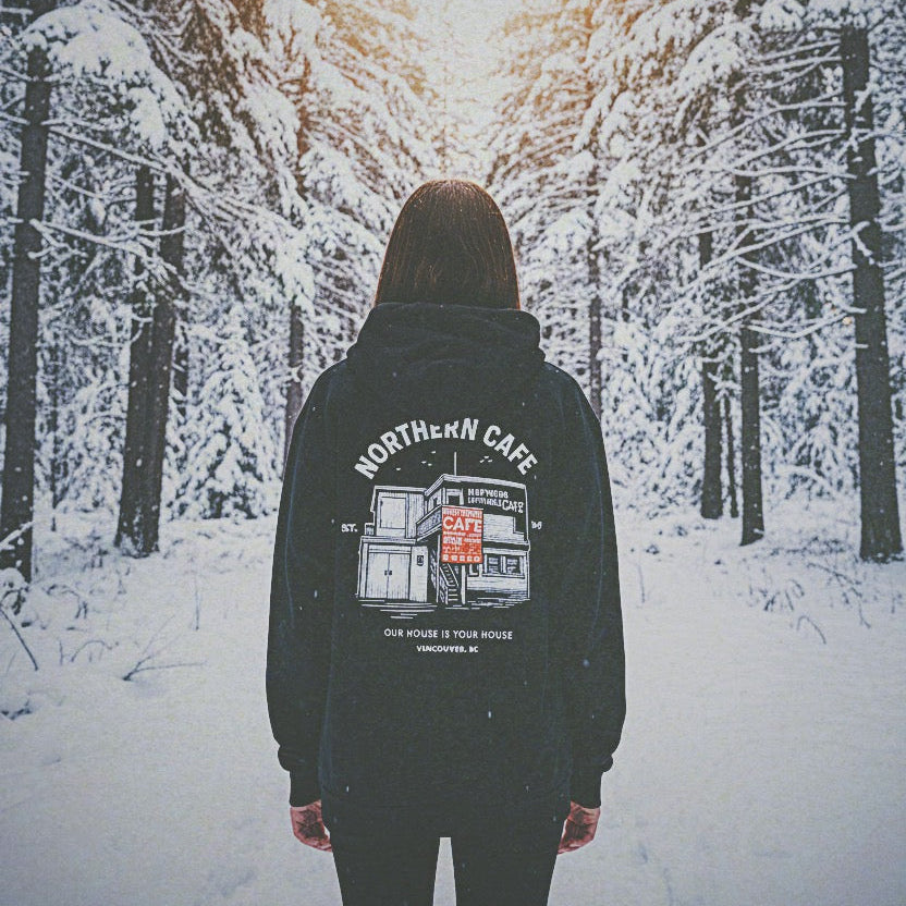 Person wearing a hoodie with 'Northern Cafe' design in a snowy forest