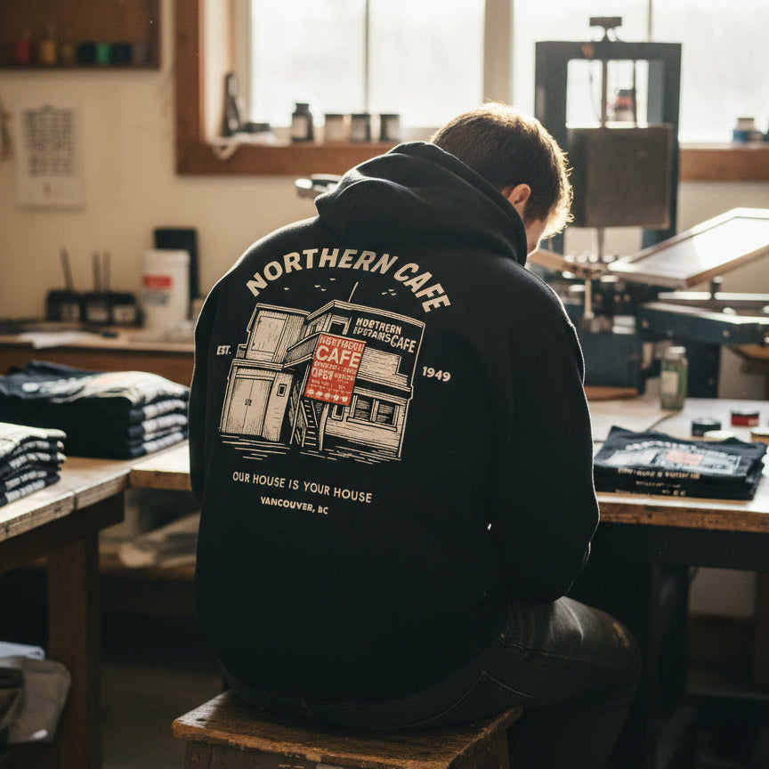 Person wearing a hoodie with 'Northern Cafe' design in a workshop setting