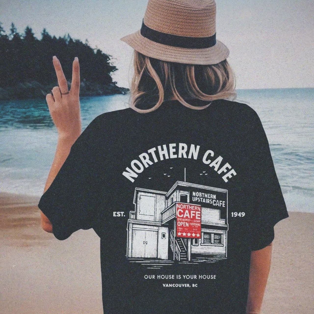 Person wearing a black t-shirt with 'Northern Cafe' design on a beach