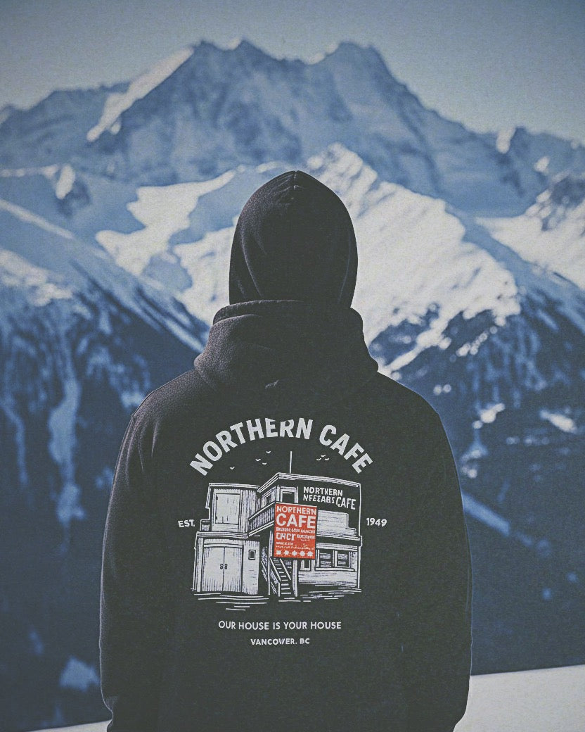 Person wearing a hoodie with 'Northern Cafe' design in front of a mountainous landscape